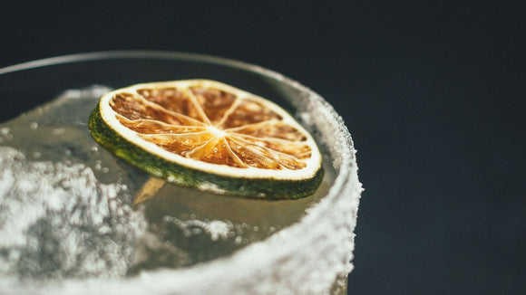 Close-up of a cocktail glass garnished with a dehydrated lime wheel and an edible flower, showcasing the Garnish & Graze collection